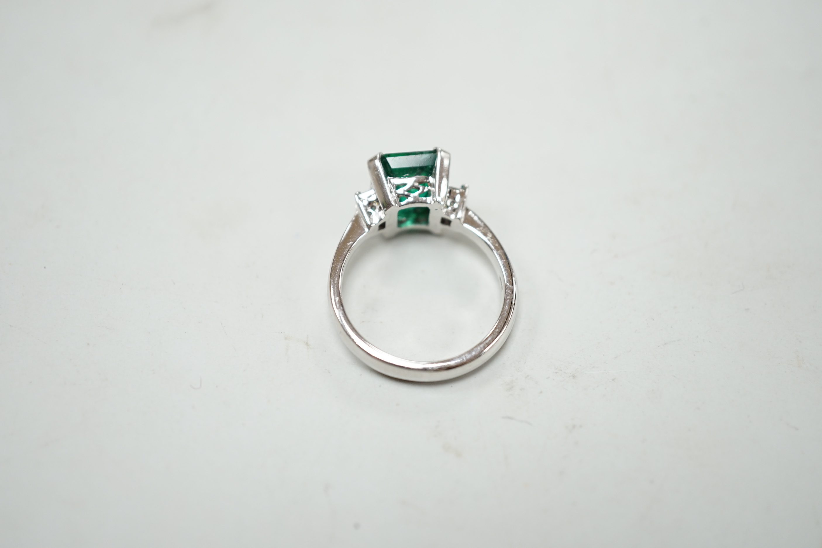 A modern 18k white metal and single stone emerald set ring, baguette cut diamond set shoulders, size N, gross weight 5.8 grams